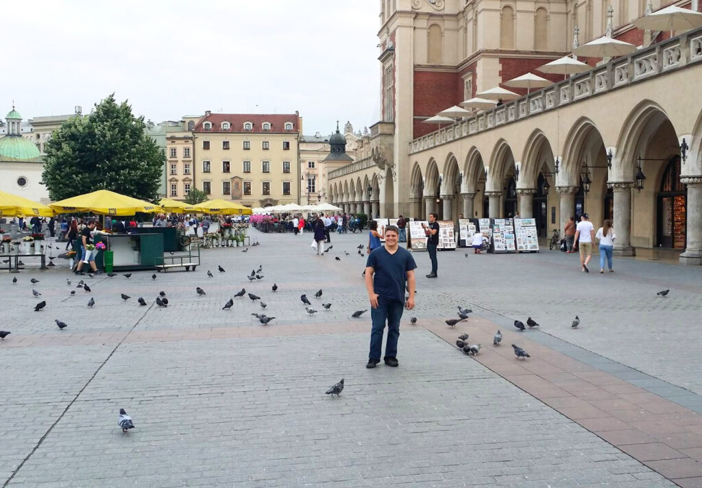 jeremy storm standing in main market square, one of the best places in krakow to visit. cloth hall is visible behind him
