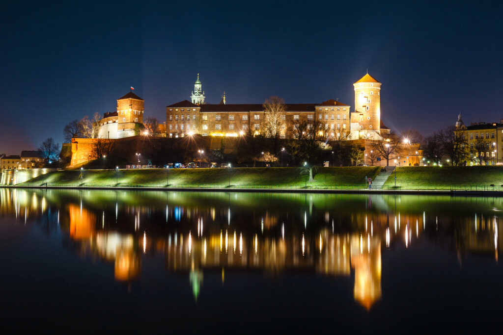 view of wawel castle lit up at night as seen from vistula river, one of the best things to see in krakow poland