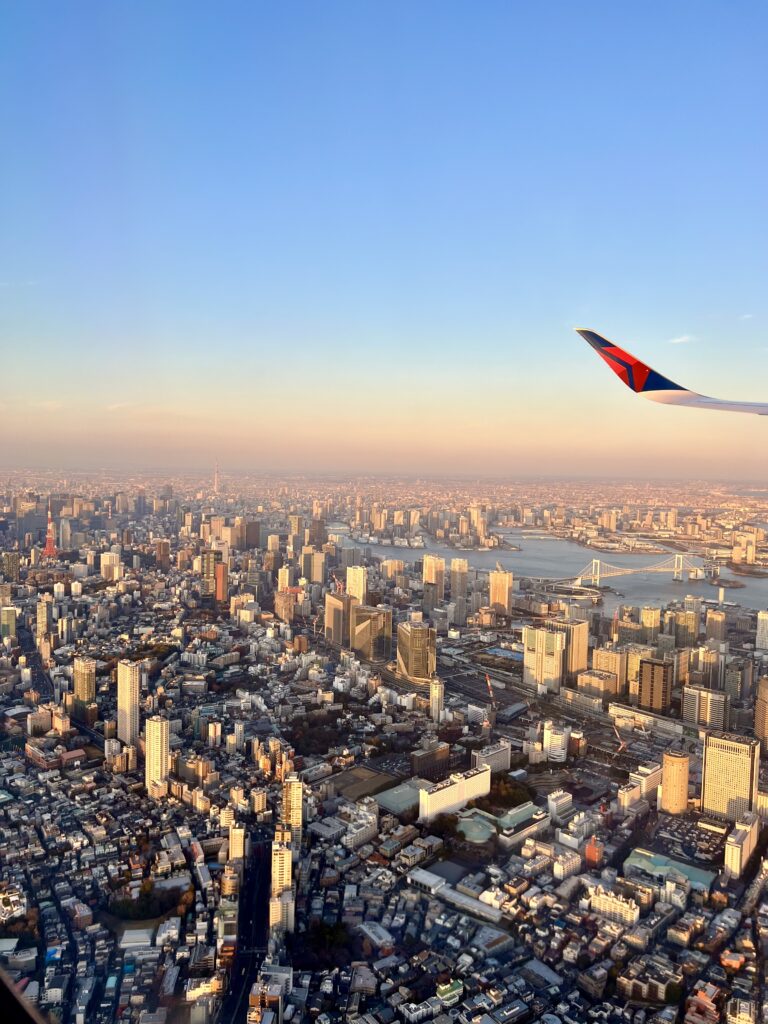 view of tokyo skyline from above as flight approaches near sunset, wing of plane visible on the right side