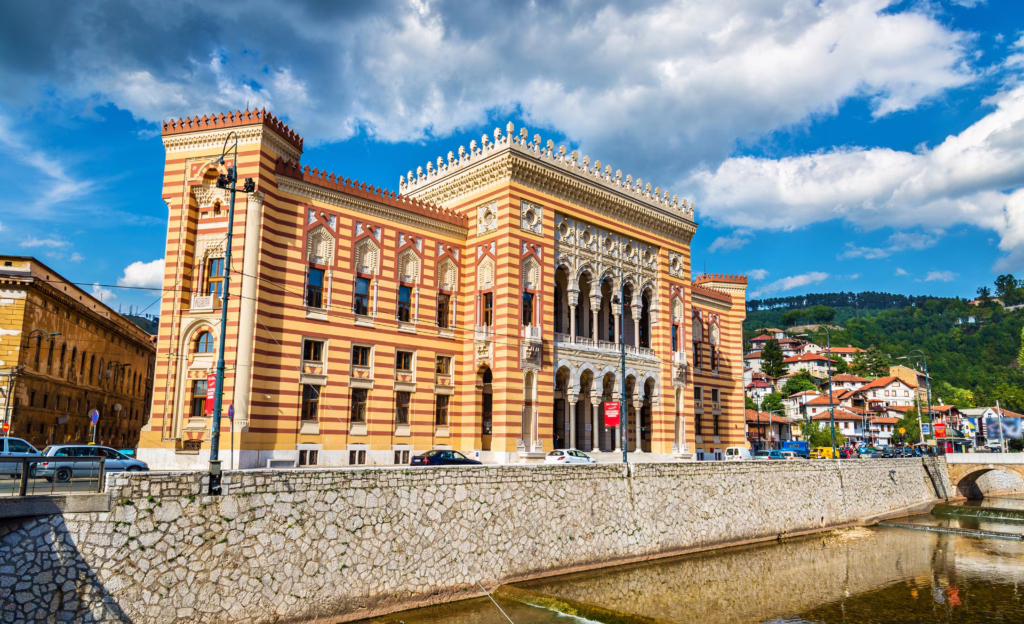 sarajevo city hall on a partly cloudy day, as seen from a slight distance. orange building that is one of the best places to visit in sarajevo bosnia and herzegovina