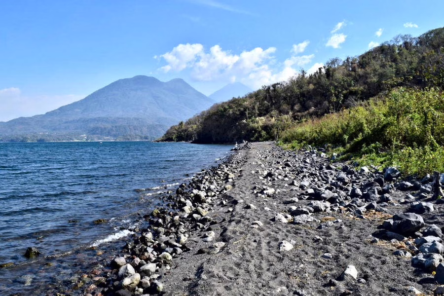 rocky shore of lake atitlan guatemala with water to the left and a volcano visible in the distance