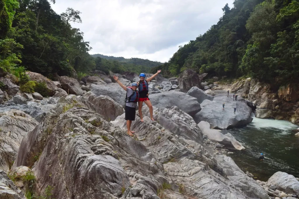 kate storm and jeremy storm holding their arms up, standing on a boulder during a whitewater rafting excursion la ceiba honduras
