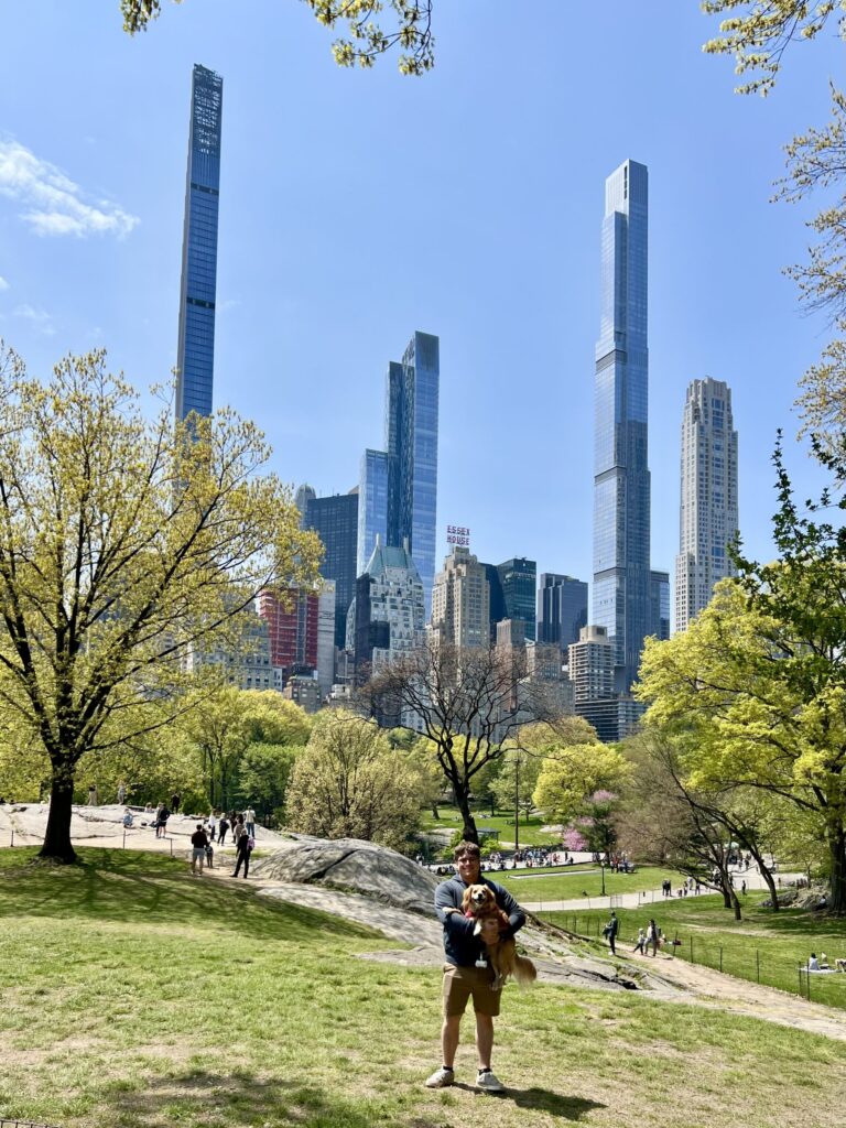jeremy storm holding his yellow dog ranger in southeast central park new york city with skyscrapers visible behind him