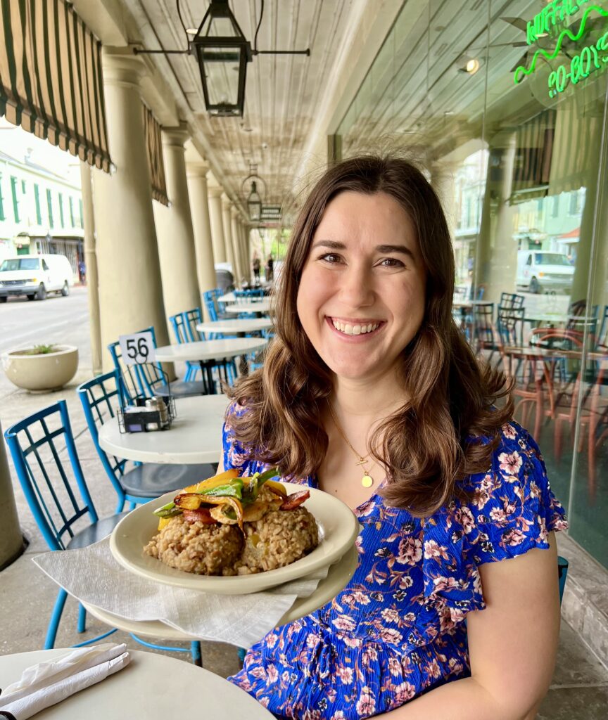 kate storm in a blue dress holding up a plate of jambalaya during a long weekend in new orleans itinerary
