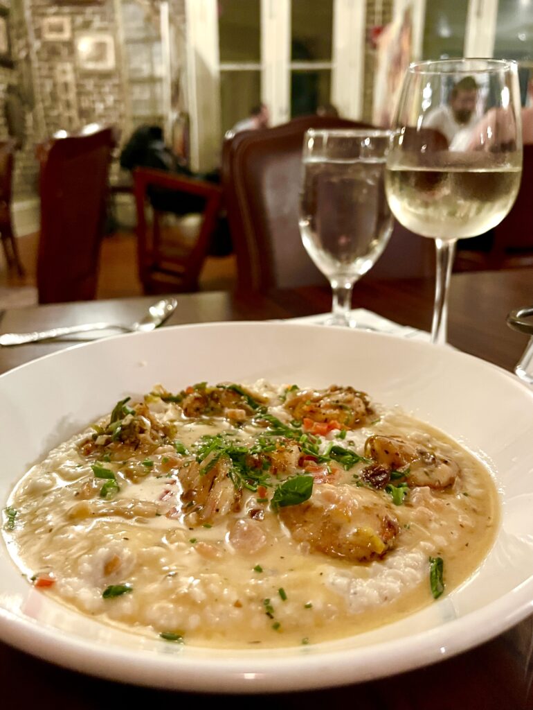 shrimp and grits on the table with a glass of white wine in muriels, one of the best restaurants in new orleans to visit