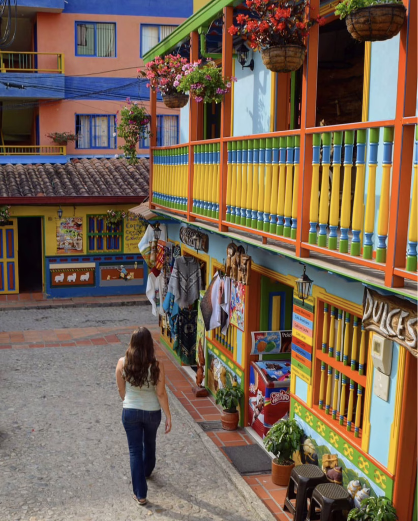 kate storm in jeans and a blue tank top walking along colorfully painted buildings when visiting guatape colombia