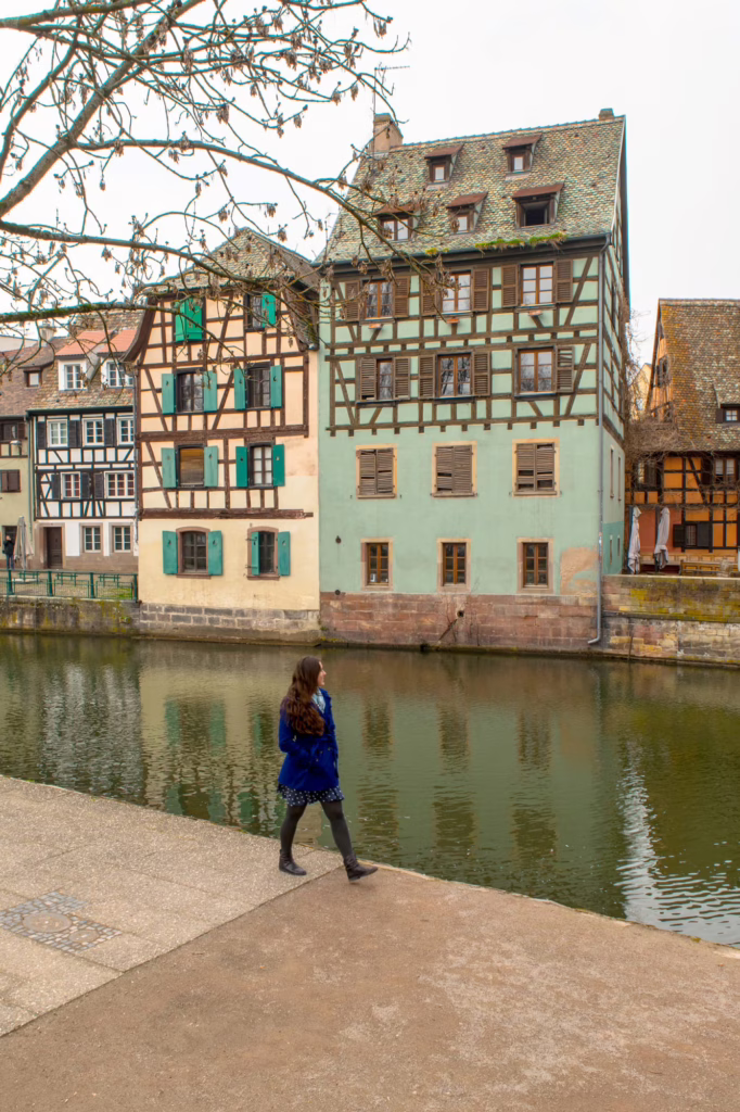 Kate Storm in a blue coat walking along a canal in La Petite France in Strasbourg in winter