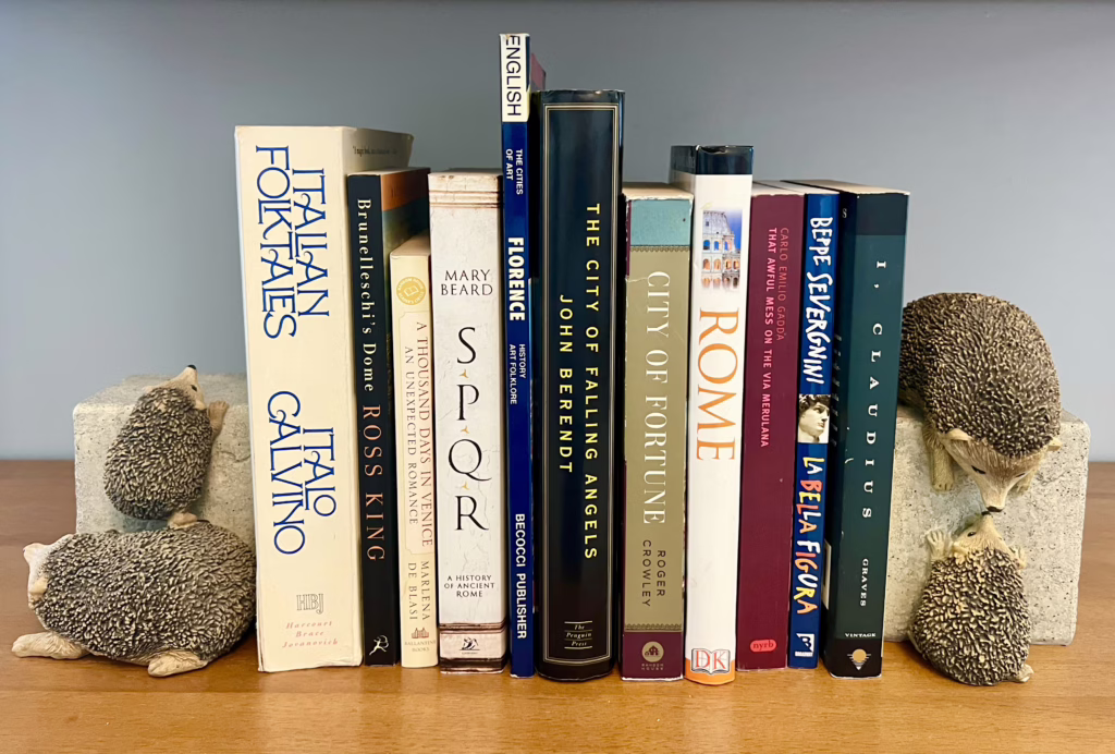 collection of the best books about italy on a bookshelf with hedgehog bookends on either side of the books