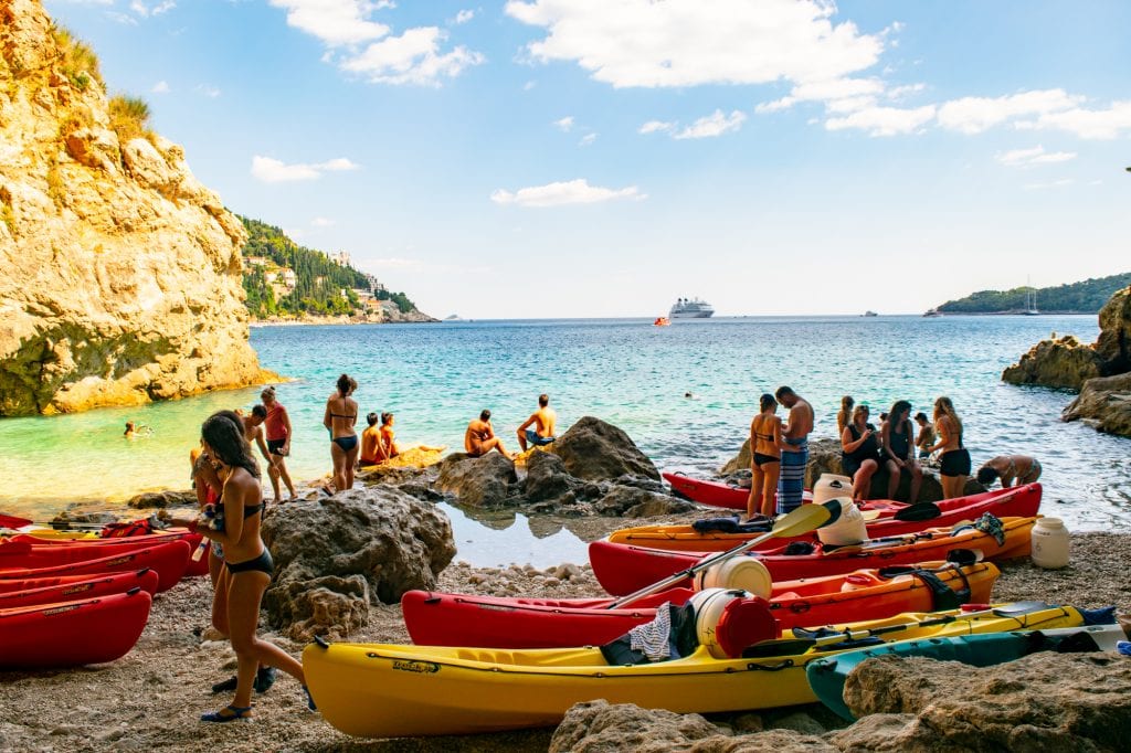 collection of travelers with grounded kayaks on a rocky shore, getting ready to swim near dubrovnik croatia