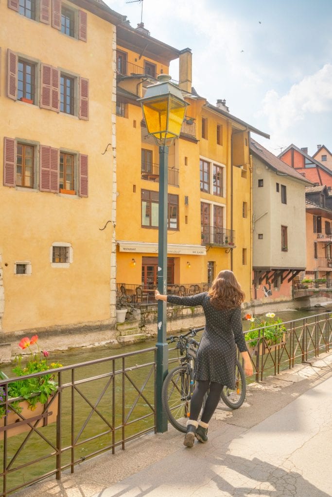kate storm holding onto a light pole and leaning to the side next to a canal when visiting annecy france