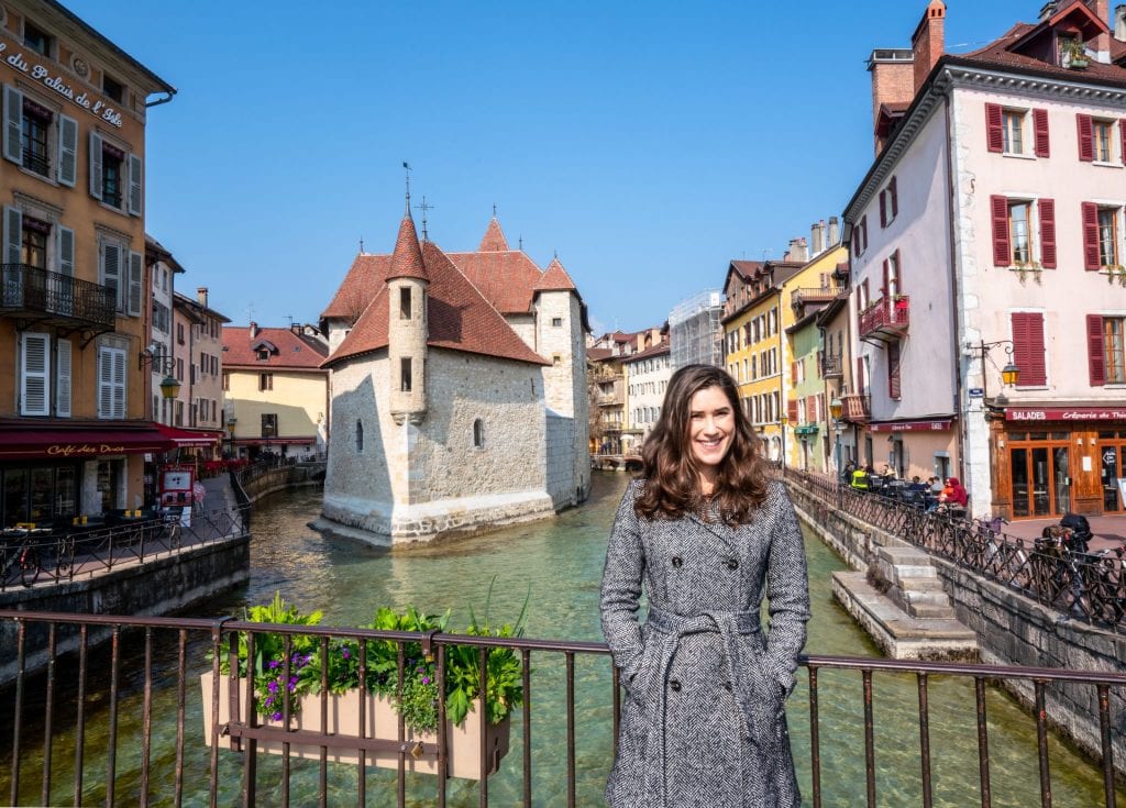 kate storm in a gray coat standing in front of the palais d'isle and canal, one of the best things to see in annecy france