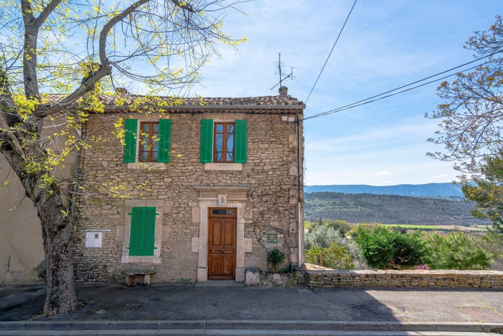 small stone house with green shutters on the edge of goult provence france