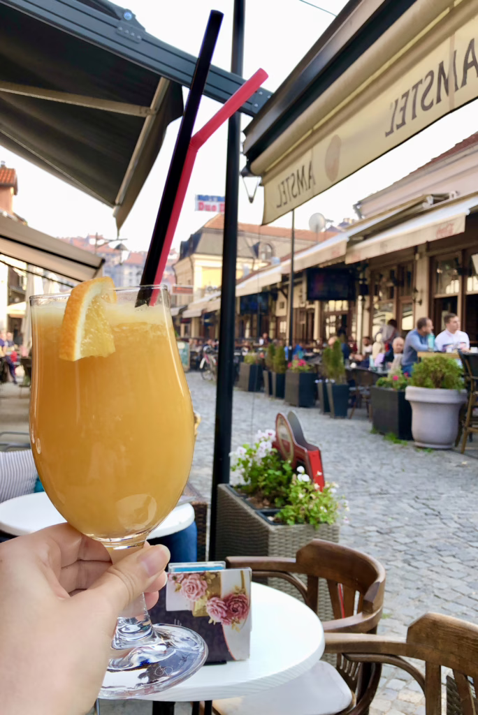 photo of a glass of orange juice being held up at a sidewalk cafe in historic center of nis serbia