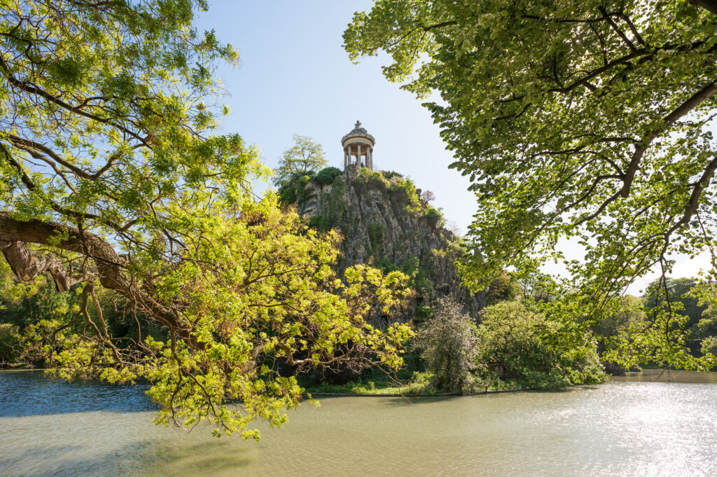 view of Temple de la Sibylle in parc des buttes chaumonts as seen from across the lake in paris france