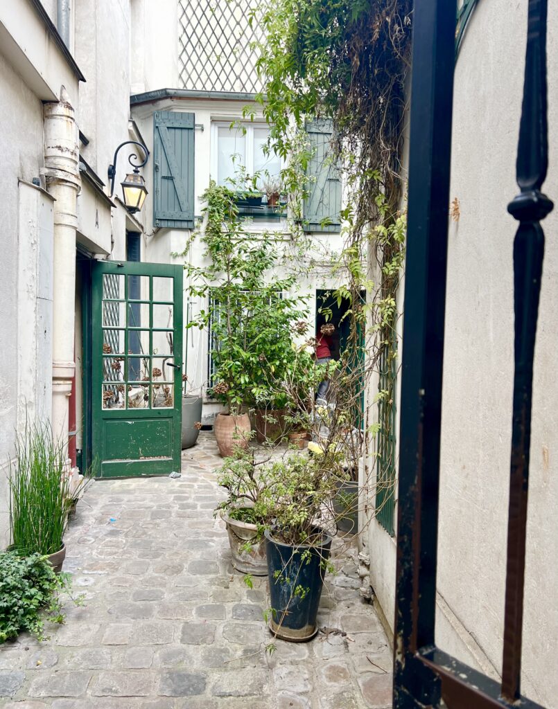 small cobblestone courtyard off of Rue du Faubourg Saint-Antoine in paris with plants and green door