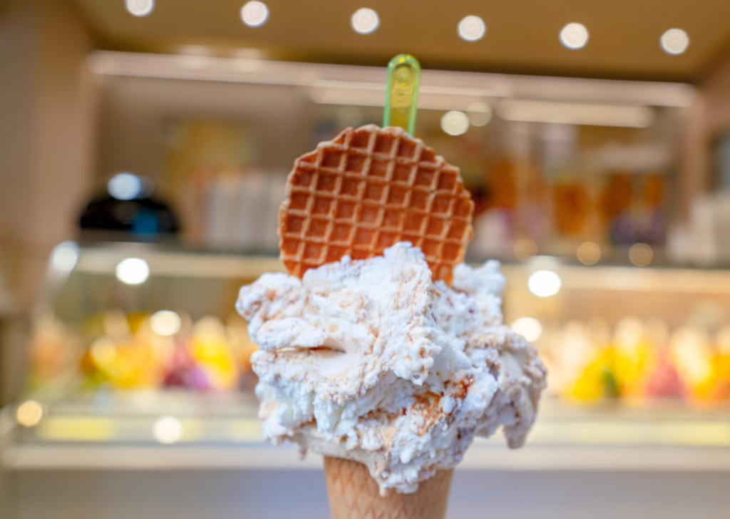 Cone of gelato with a cookie stuck in it held in front of a gelato counter.