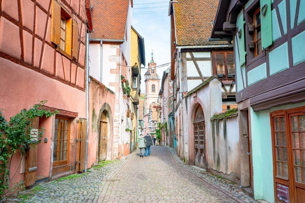 cobblestone street in riquewihr france lined by colorful half timbered buildings on either side
