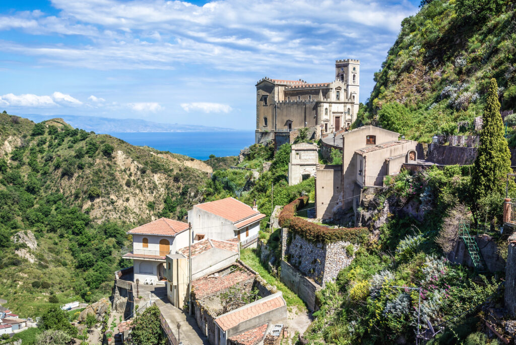 view of savoca sicily village from afar with church prominent on the edge of a cliff