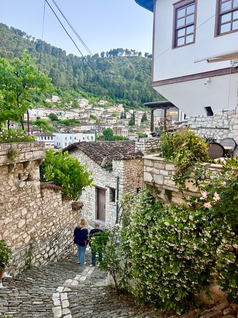 cobblestone streets of berat albania with ottoman style building to the right, street is leading downhill with cliff visible in the background