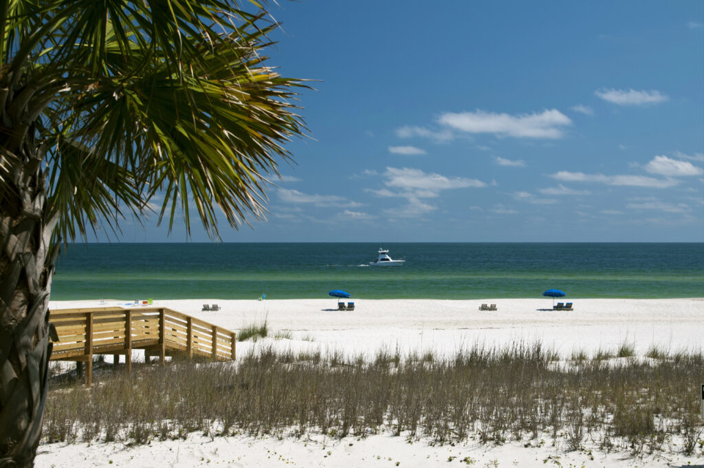white sand beaches of alabama as seen from behind the dunes, with a boat visible on the water