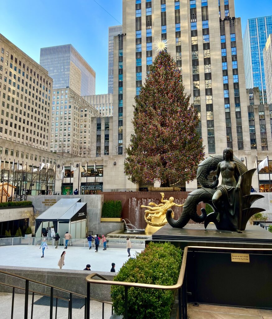 photo of rockefeller christmas tree in new york city taken from the side on a sunny day with ice skating rink visible toward the bottom