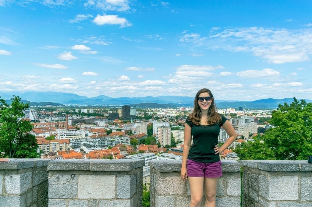 kate storm standing at the edge of ljubljana slovenia castle grounds, with city visible behind her