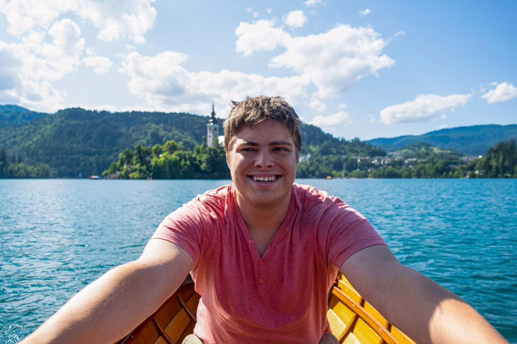 Jeremy Storm rowing a small wooden boat in Lake Bled slovenia, wearing a melon colored shirt
