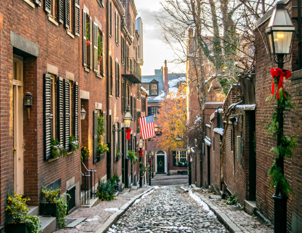 acorn street in beacon hill boston at christmas, with a little bit of snow on the ground and wreaths on the buildings and light poles