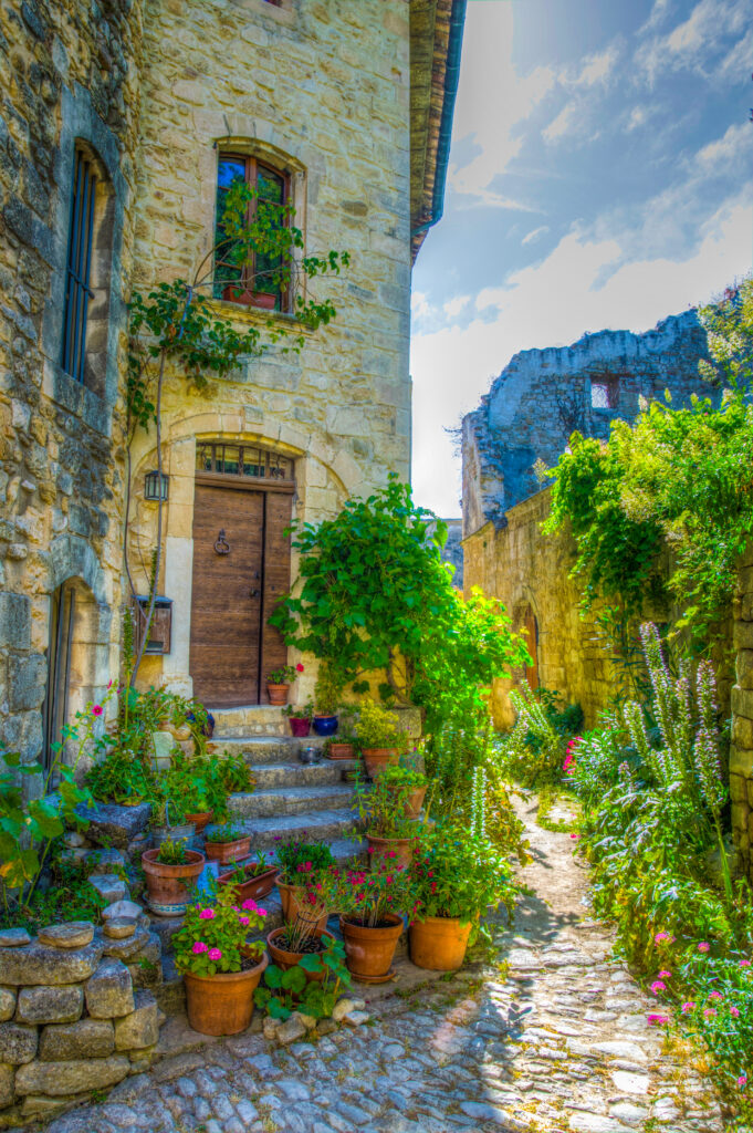 stone buildings along a narrow cobblestone street in oppede le vieux france, with potted plants in front of a doorway to one side