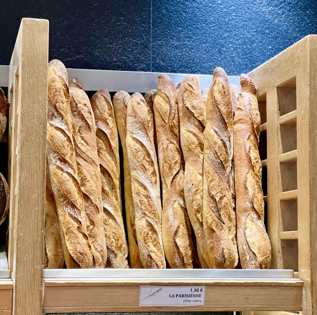 collection of freshly baked baguettes on a shelf that are for sale in a parisian boulangerie