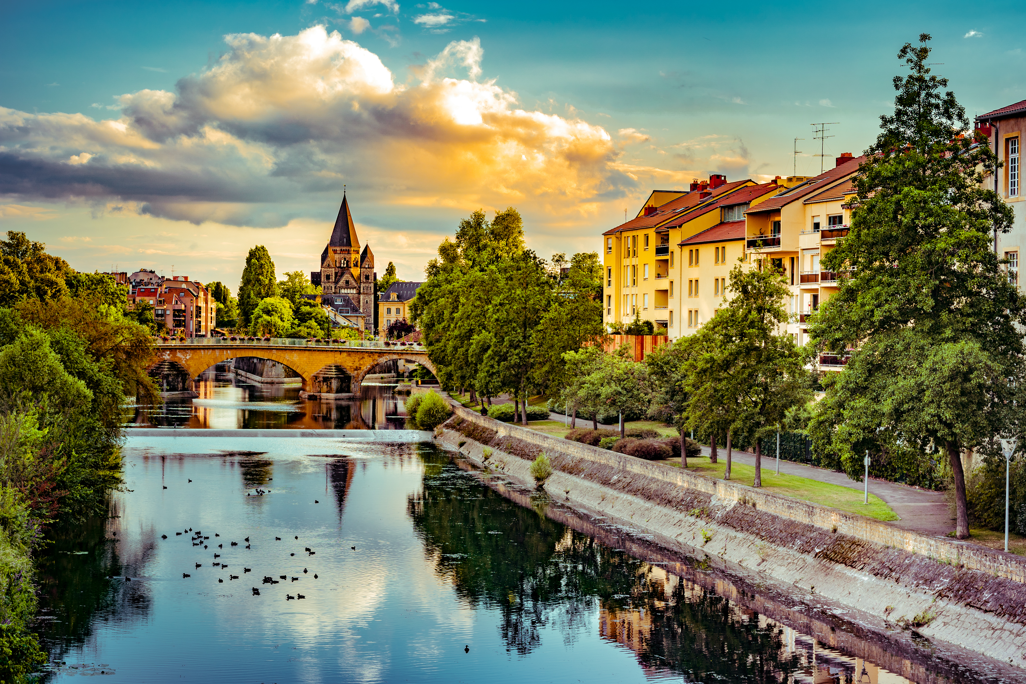 photo of metz france at sunset with river in the foreground and temple neuf visible in the distance