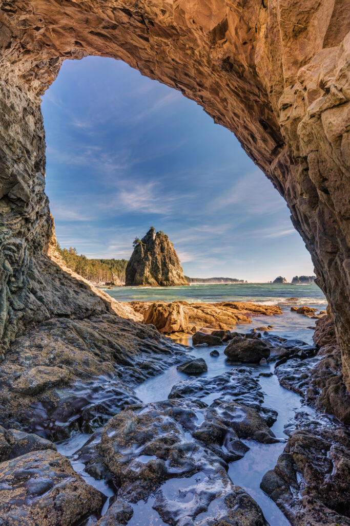 view of rialto beach through hole in the wall cliff on a sunny day, one of the best stops on a pnw road trip west coast usa