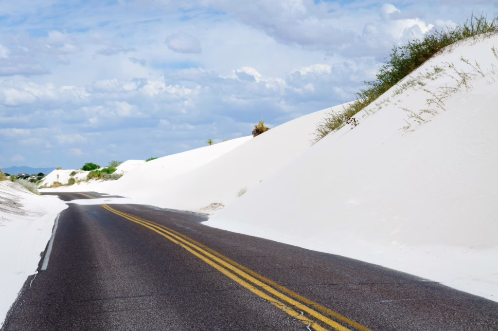 two lane road in white sands national park, surrounded by white sand dunes on either side