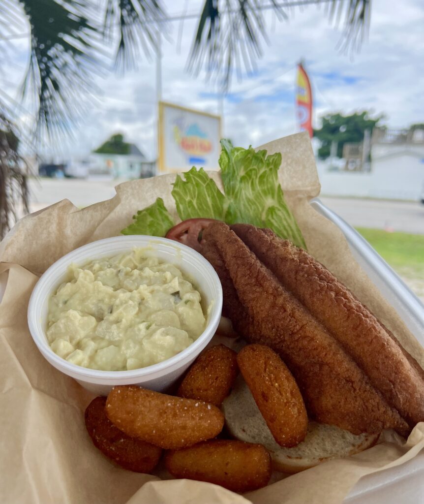 basket of fried fish with hush puppies and potato salad being held up in front of the shark shack sign, a popular atlantic beach seafood restaurant