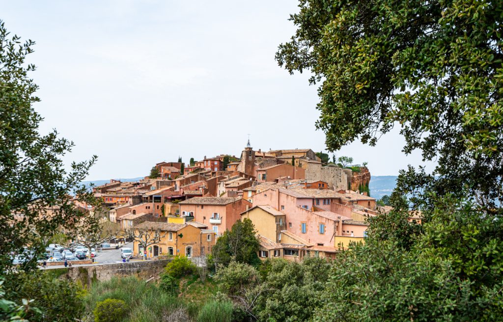 view of roussillon luberon provence town through the trees as seen from trail outside of town, one of the best towns in france to visit
