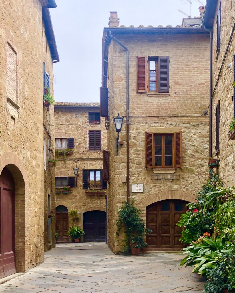 courtyard in pienza tuscany with brown buildings with potted plants outside of them