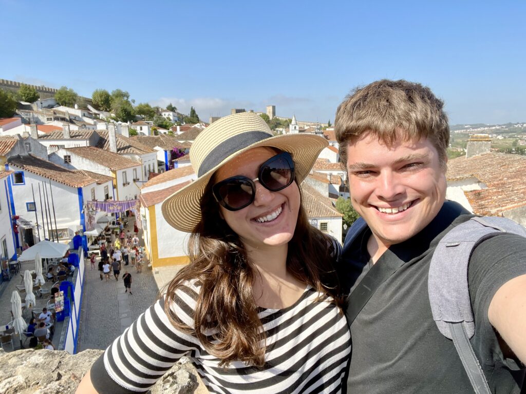 kate storm and jeremy storm taking a selfie on the obidos town walls when visiting obidos portugal, the whitewashed buildings of the town visible behind them