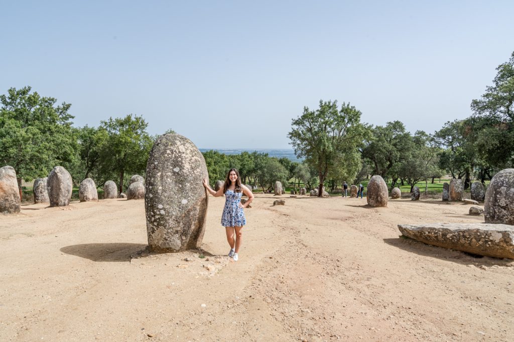 kate storm holding her hand up to a megalith structure near evora portugal, one of the coolest hidden places in europe to visit