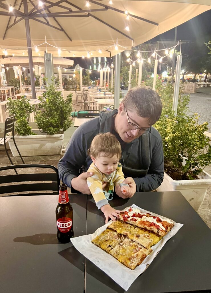 jeremy storm and his baby with a plate of pizza al taglio at a table in tivoli italy