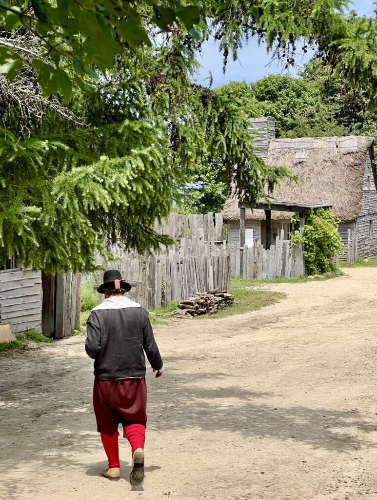 man dressed as a pilgrim walking across the dirt road in the 17th century english village at the plimoth patuxet museums on a day trip to plymouth from boston
