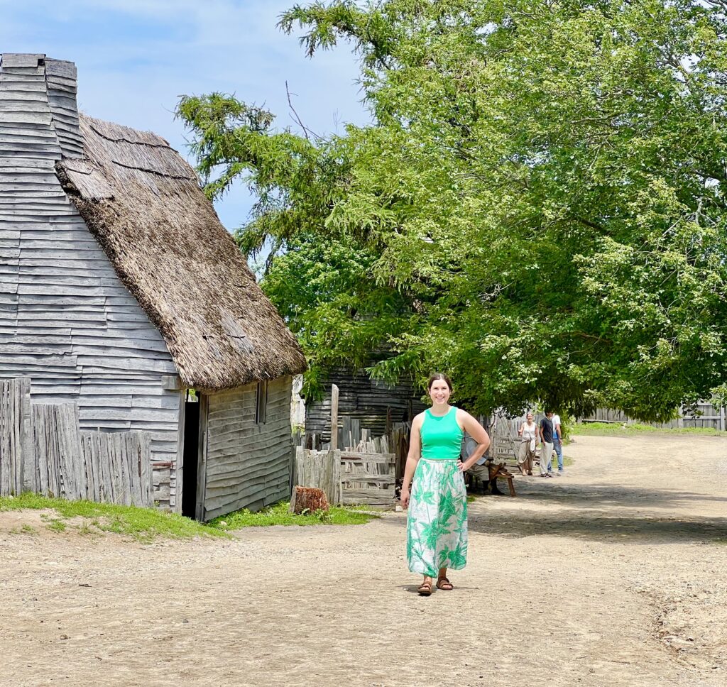 kate storm standing in the dirt road at the plimouth patuxet museums next to a cabin, in plymouth, one of the best day trips from boston ma