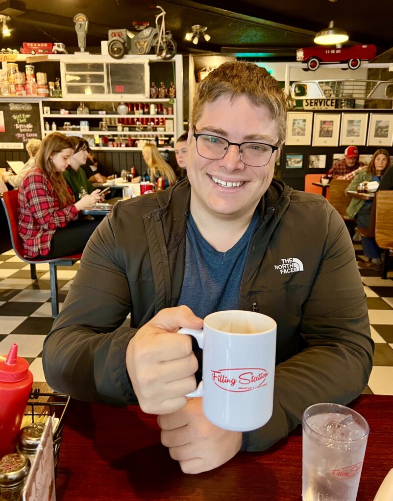 jeremy storm holding up a cup of coffee while seated at the filling station restaurant in eureka springs arkansas