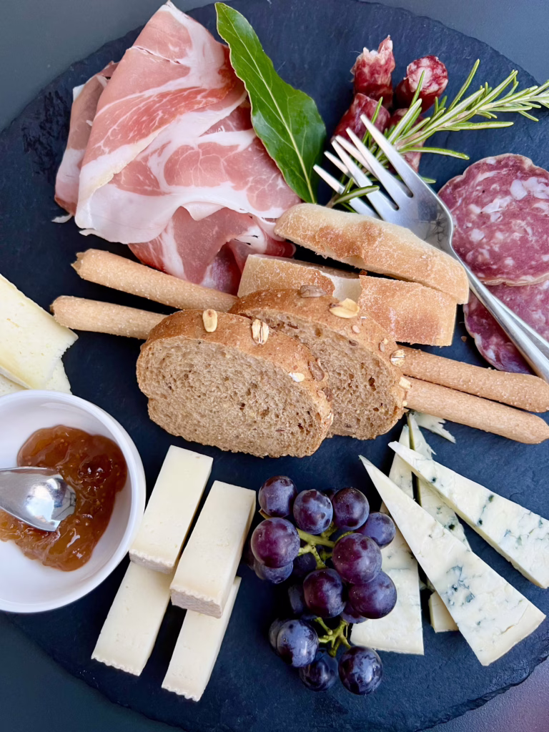 photo of cheese and cured meat plate from above with bread and herbs, served with barolo wine at a wine bar in piedmont italy