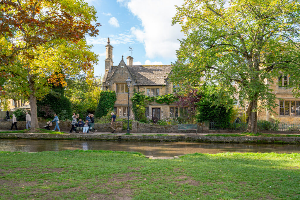 photo of river windrush and traditional stone building behind a green lawn as seen on a visit bourton on the water england