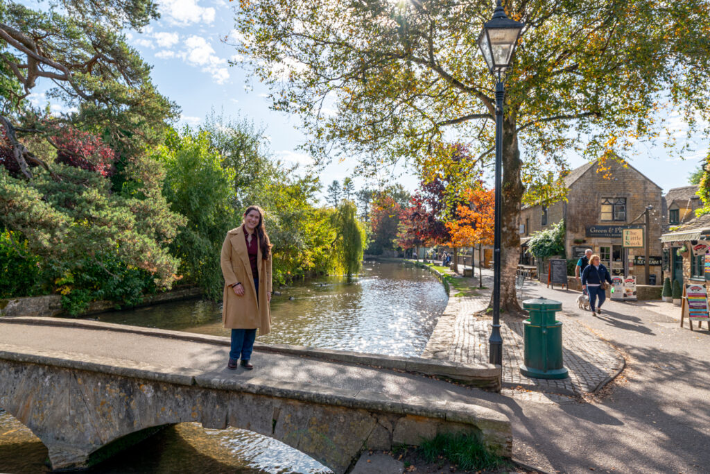 kate storm standing on a stone bridge over the river windrush, one of the best things to do in bourton on the water england cotswolds