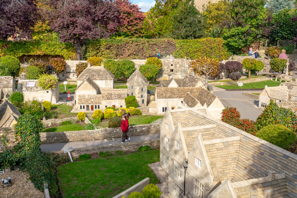 bourton on the water model village as seen from above with a toddler in red walking through it