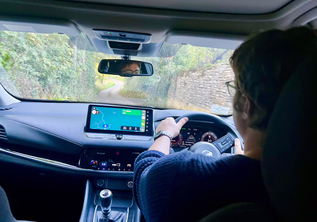 photo taken from back seat of car showing jeremy storm driving on a narrow road in the cotswolds