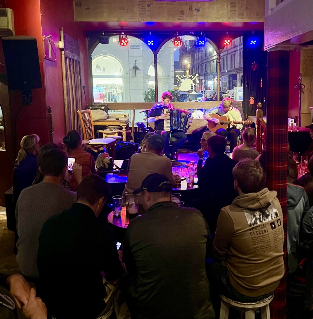 group of people in hootananny pub in inverness scotland watching 2 performers seated against a window