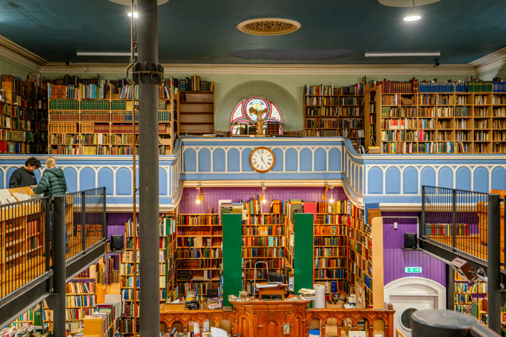 interior of leakeys bookshop with clock on a blue wall in the center and crowded bookshelves surrounding it, visiting is one of the top things to do in inverness scotland