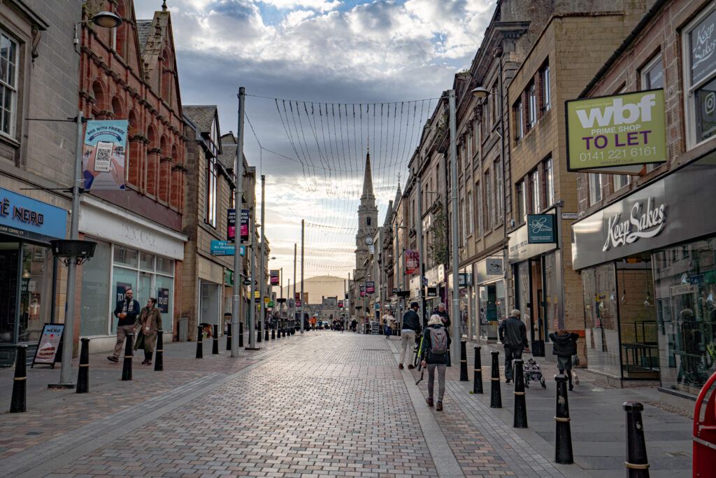 view of cobblestone street in inverness city center with shops lining the street and a steeple visible in the background